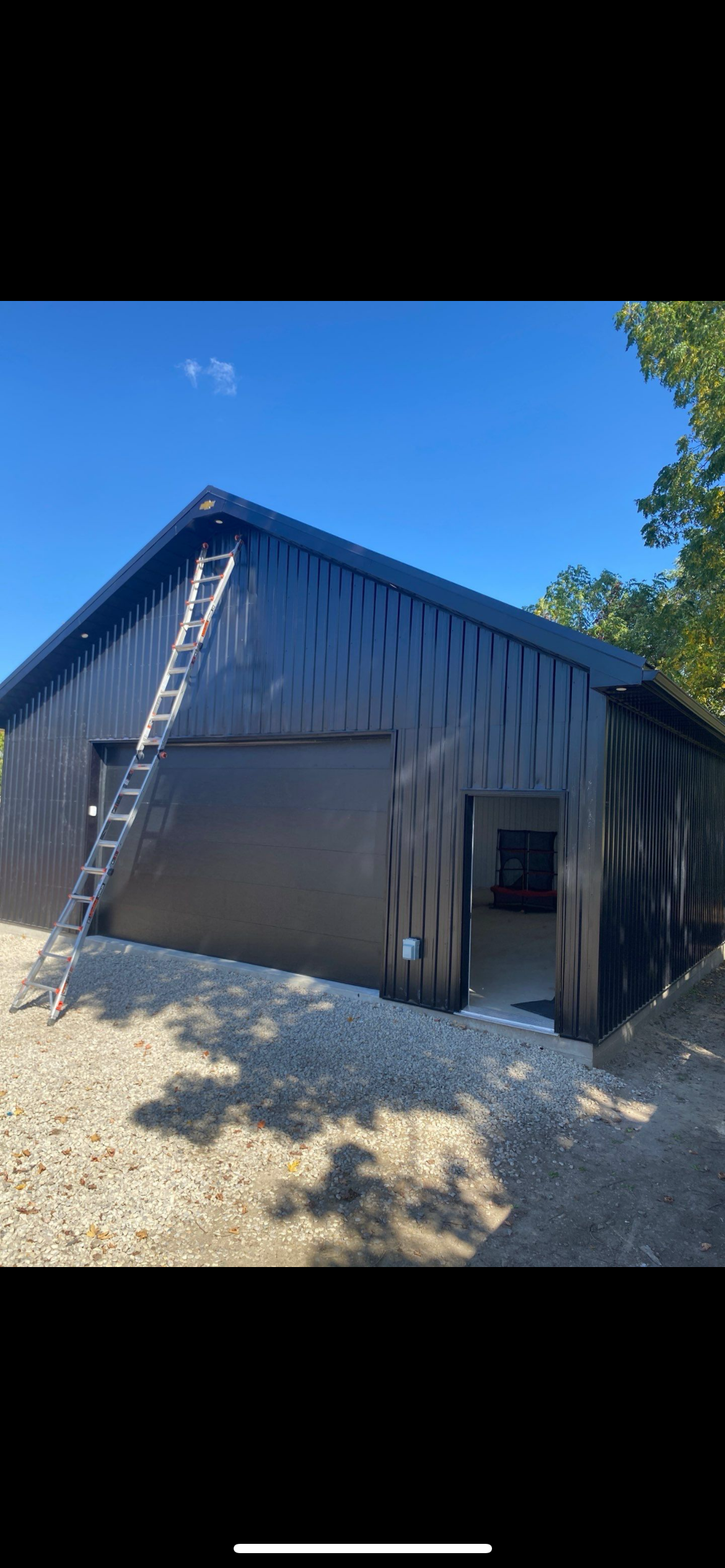 Black steel structure shop with large roll-up door and ladder — front view